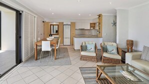 A modern living room with a dining area, kitchen, and a glass door leading to a balcony. - Illawong 1 Beachfront Doorstep Apt (Mooloolaba)