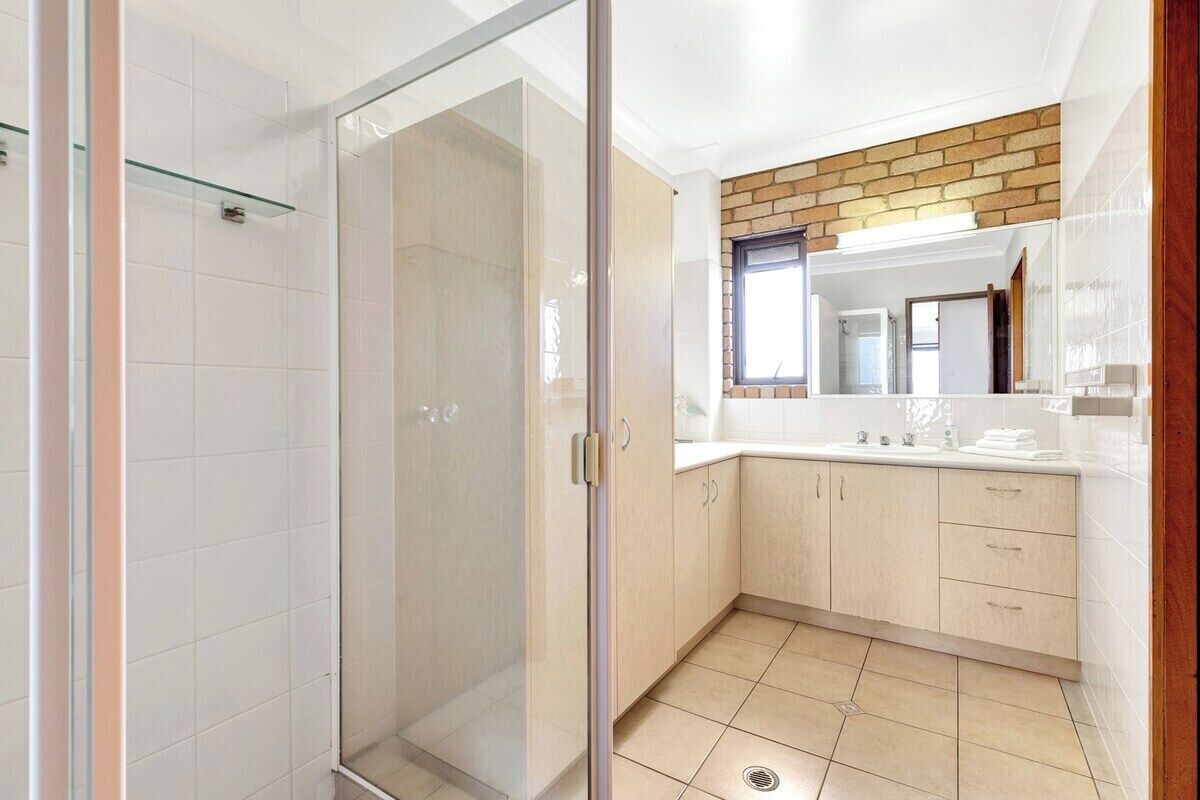 Une salle de bain moderne avec une douche à parois de verre, un espace de douche carrelé de carreaux blancs, un lavabo avec un miroir au-dessus et des meubles de couleur claire.