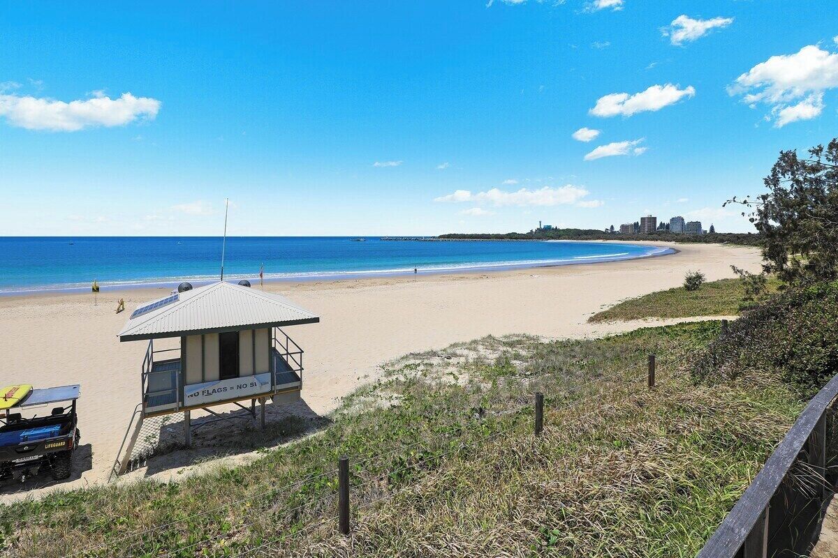 A lifeguard tower on a beach with a clear view of the ocean and distant buildings.