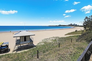 A lifeguard tower on a beach with a clear view of the ocean and distant buildings.