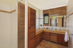 Een badkamer met een houten wastafelmeubel, een wastafel, een spiegel en een douchehoek.