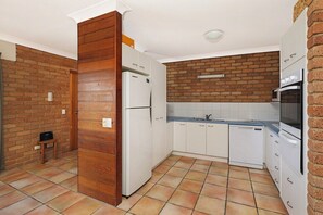 A compact kitchen with white cabinets, a brick wall, and a tiled floor.