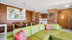 Ein modernes Wohnzimmer mit einem grünen Ledersofa, einem Essbereich mit Holztisch und -stühlen sowie einer Küche im Hintergrund.