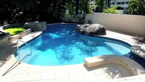 Une piscine à bord incurvé, entourée d’une terrasse carrelée et d’un petit muret.