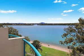 Une vue sur un lac avec une plage, une montagne à l’horizon et un bâtiment doté d’un balcon.