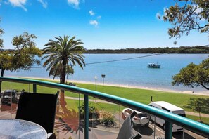 Un balcon avec vue sur un lac, un bateau et un fourgon blanc garé sur la rive.
