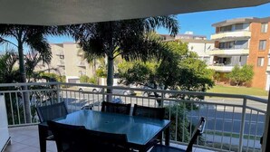 Un balcon avec une table et des chaises, une balustrade et une vue sur des immeubles et des arbres.