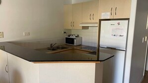 Une cuisine avec un plan de travail noir, un four à micro-ondes, un réfrigérateur et des armoires de couleur beige.