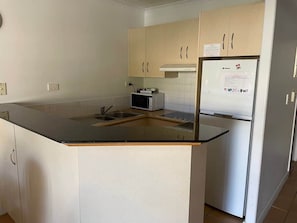 A kitchen with a black countertop, a microwave, a refrigerator, and beige cabinets. - 2BR Alex Beach Resort Apt Near Beach 317 (Alexandra Headland)