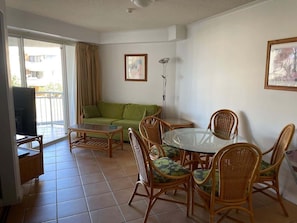 A living room with a green sofa, wicker chairs, a glass-top table, and a TV. - 2BR Alex Beach Resort Apt Near Beach 317 (Alexandra Headland)