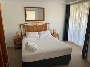 A hotel room with a large bed, a wooden headboard, two bedside tables with lamps, a mirror above the bed, and a window with curtains. - 2BR Alex Beach Resort Apt Near Beach 317 (Alexandra Headland)