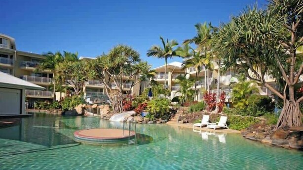 Une piscine d’hôtel avec une eau cristalline, entourée de palmiers et de chaises longues.
