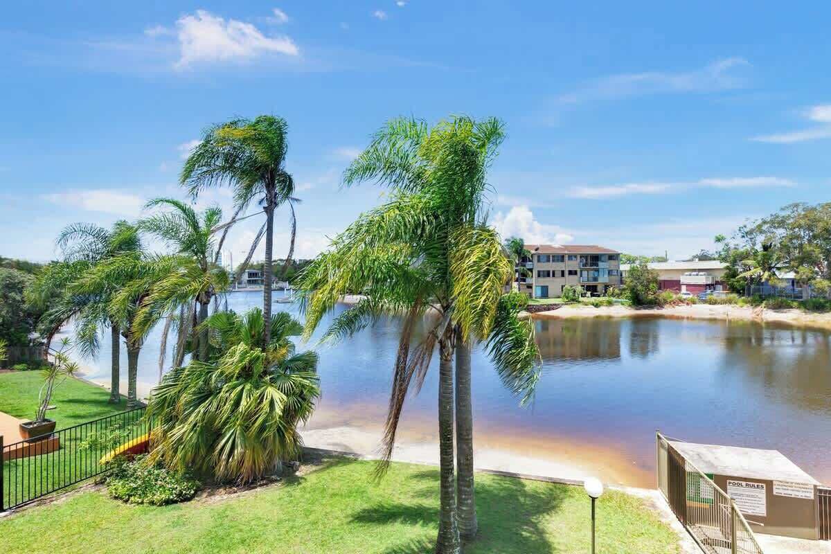 A resort with palm trees, a body of water, and a building in the background.