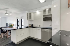 A modern kitchen with white cabinetry, a black countertop, and a built-in dishwasher. - Hacienda 3 Canal View Comfort Apt (Mooloolaba)