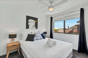 Een hotelkamer met een bed, nachtkastje met lamp, plafondventilator, raam met gordijnen en een kunstwerk aan de muur.