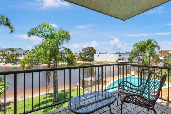 Een balkon met uitzicht op een zwembad, palmbomen en een rivier.
