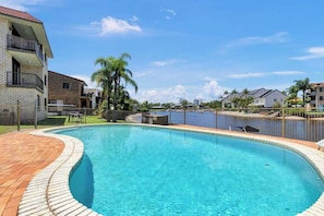 Una piscina con plataforma de ladrillo, rodeada de edificios residenciales y una masa de agua.