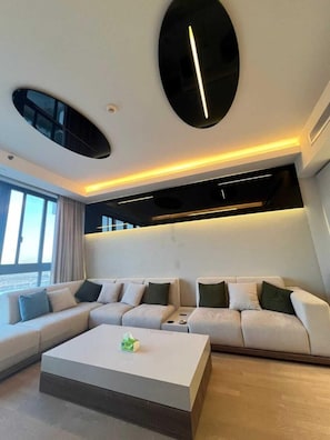 A modern living room with a sectional sofa, a coffee table, and a large window providing a view. - Luxury Chic Suite In Aeon Compound- Mall Of Arabia Towers (Giza Governorate)