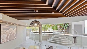 A modern interior with a long dining table, wicker chairs, a large artwork, and a staircase leading to an outdoor area. - Breeze 801 Luxury Mooloolaba Apt with Ocean Views (Mooloolaba)