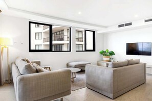 A modern living room with a sofa, a TV, and a large window with a balcony view. - Breeze 801 Luxury Mooloolaba Apt with Ocean Views (Mooloolaba)