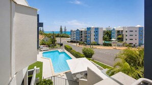 Un edificio residencial con piscina, una calle y otros edificios al fondo.