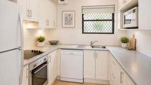 Cocina moderna con armarios blancos, lavavajillas, horno, microondas, pileta y ventana con mosquitero.