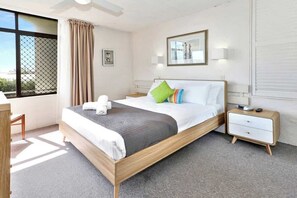 Ein Schlafzimmer mit Bett, Nachttischen, einem Schreibtisch, einem Fenster mit Vorhängen und einem gerahmten Bild an der Wand.