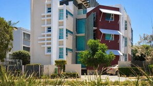 Ein modernes Mehrfamilienhaus mit Balkonen, ein Auto vor der Fassade und umliegendes Grün.