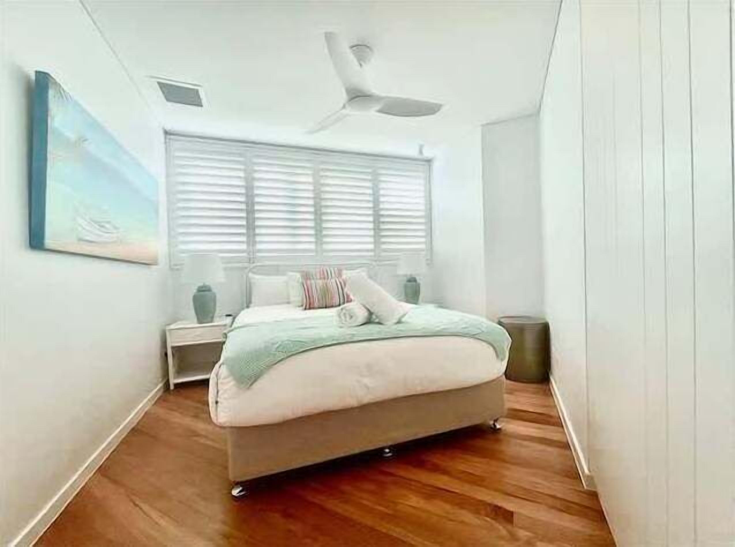 A bedroom with a bed, a ceiling fan, a nightstand, and a window with blinds.