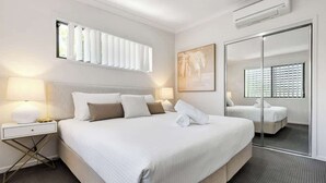 A hotel room with a large bed, bedside lamps, a mirror, and a window with blinds.