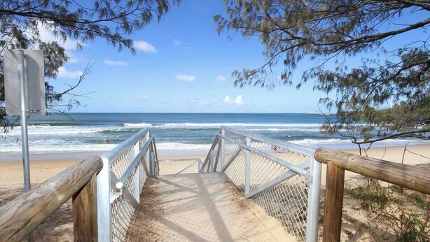 A beach walkway leading to the ocean with a metal railing and wooden posts.