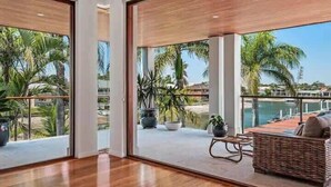 A modern interior with large windows, a wooden floor, and a wicker sofa. - Luxury Tropical Haven Mooloolaba (Mooloolaba)