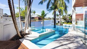 A swimming pool with clear blue water, surrounded by palm trees and a wooden deck. - Luxury Tropical Haven Mooloolaba (Mooloolaba)