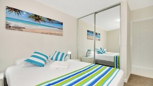 A bedroom with a bed, striped bedspread, pillows, a nightstand, a lamp, and a large mirror.