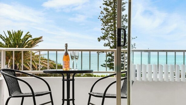 A balcony with a table and two chairs, overlooking a beach.
