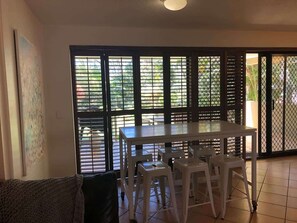 Une pièce comprenant une table à manger et des chaises, un canapé, et offrant une vue sur l’extérieur grâce à de grandes fenêtres à carreaux.