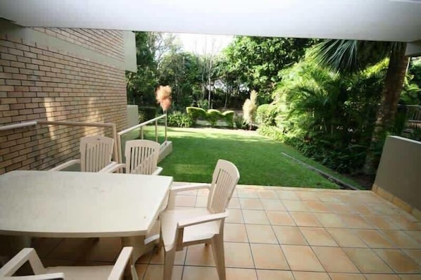 A patio with a table and chairs, a brick wall, and a view of a well-maintained garden.