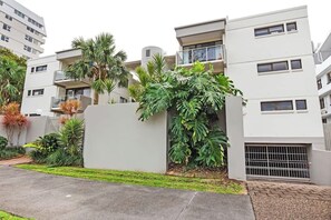 Un immeuble résidentiel à plusieurs étages, doté de balcons, d’une entrée sécurisée et d’une végétation luxuriante.