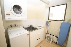 A compact laundry area with a washing machine, a sink, a drying rack, and a fan.