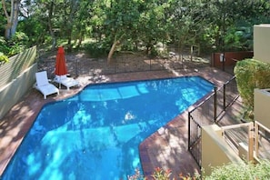 Une piscine avec une terrasse en bois, entourée d’une clôture, et un parasol rouge.