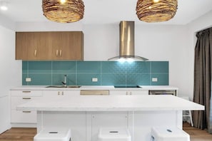 A modern kitchen with white cabinetry, teal backsplash, and a central island with stools. - Lahaina 4 Beachfront Apt Mooloolaba (Maroochydore)