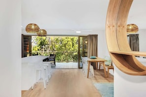 A modern interior with a dining area, white bar stools, a wooden table, and a large mirror.