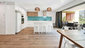 Una cucina moderna con mobili bianchi, uno schienale verde acqua e un tavolo da pranzo in legno con sgabelli bianchi.