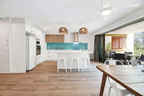 A modern kitchen with white cabinets, a teal backsplash, and a wooden dining table with white stools. - Lahaina 4 Beachfront Apt Mooloolaba (Maroochydore)