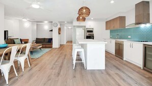 Una cucina moderna con mobili bianchi, un'isola centrale e una zona pranzo con sedie bianche.