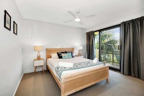 A bedroom with a bed, bedside tables, a ceiling fan, and a view through a window with curtains. - Lahaina 4 Beachfront Apt Mooloolaba (Maroochydore)