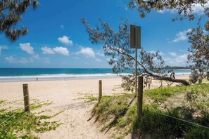 Ein Strand mit einer Holzlattenzaun, einem Wegweiser und freiem Blick auf den Ozean.