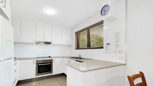 Una cocina moderna con muebles blancos, un horno de acero inoxidable, un lavaplatos y un reloj en la pared.
