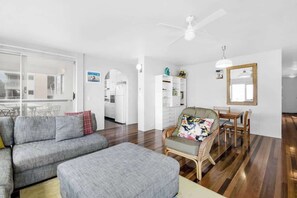 A modern living room with a sofa, ottoman, dining table, and chairs. - Headlands 16 Ocean View Holiday (Alexandra Headland)