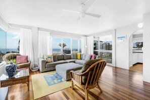 A spacious living room with a large sofa, a chair, and a view of the ocean. - Headlands 16 Ocean View Holiday (Alexandra Headland)